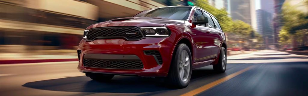 A red 2025 Dodge Durango SUV driving swiftly through a city street, surrounded by tall buildings and blurred motion in the background, emphasizing speed and urban performance.