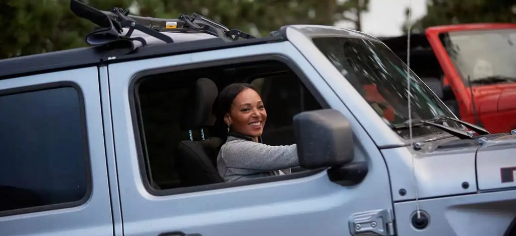 Smiling woman driving a Jeep with the soft top open, showcasing the fun and freedom of open-air driving.
