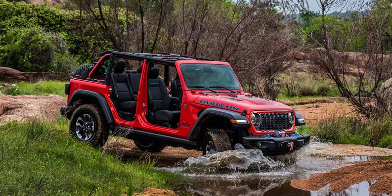 A red Jeep Wrangler Rubicon driving through a shallow stream with the doors removed.