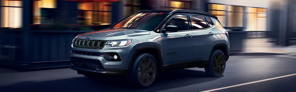 A silver Jeep Compass driving through an urban area at night.