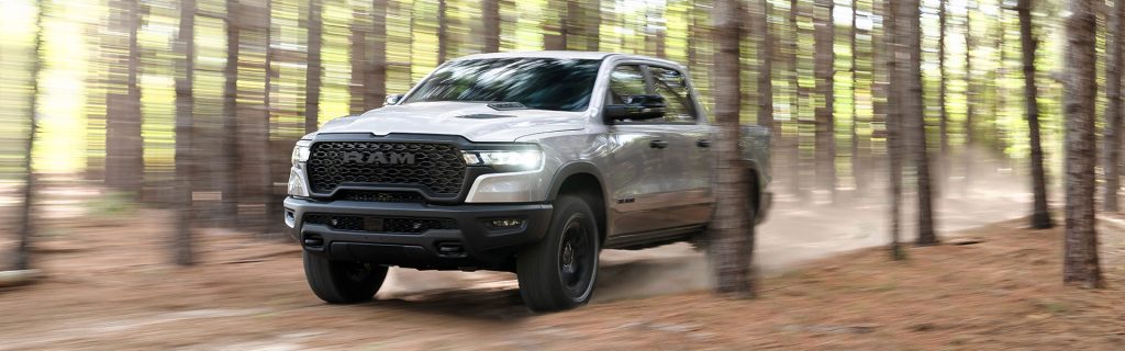 A silver RAM truck driving through a forest with blurred trees in the background.