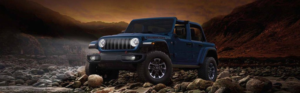 A blue Jeep Wrangler Rubicon parked on rocky terrain with dramatic lighting.